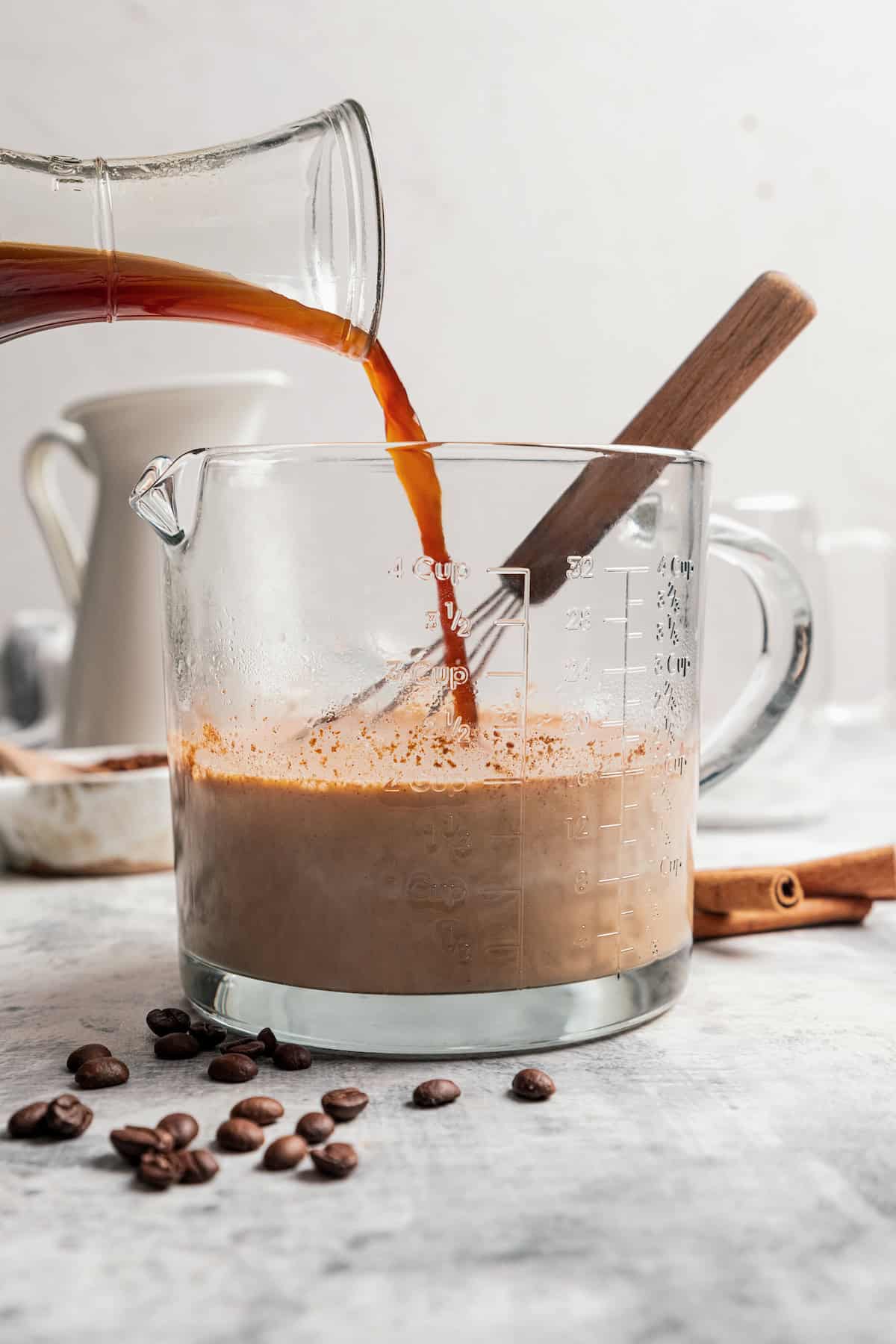 Espresso being poured into eggnog in a glass mixing bowl.