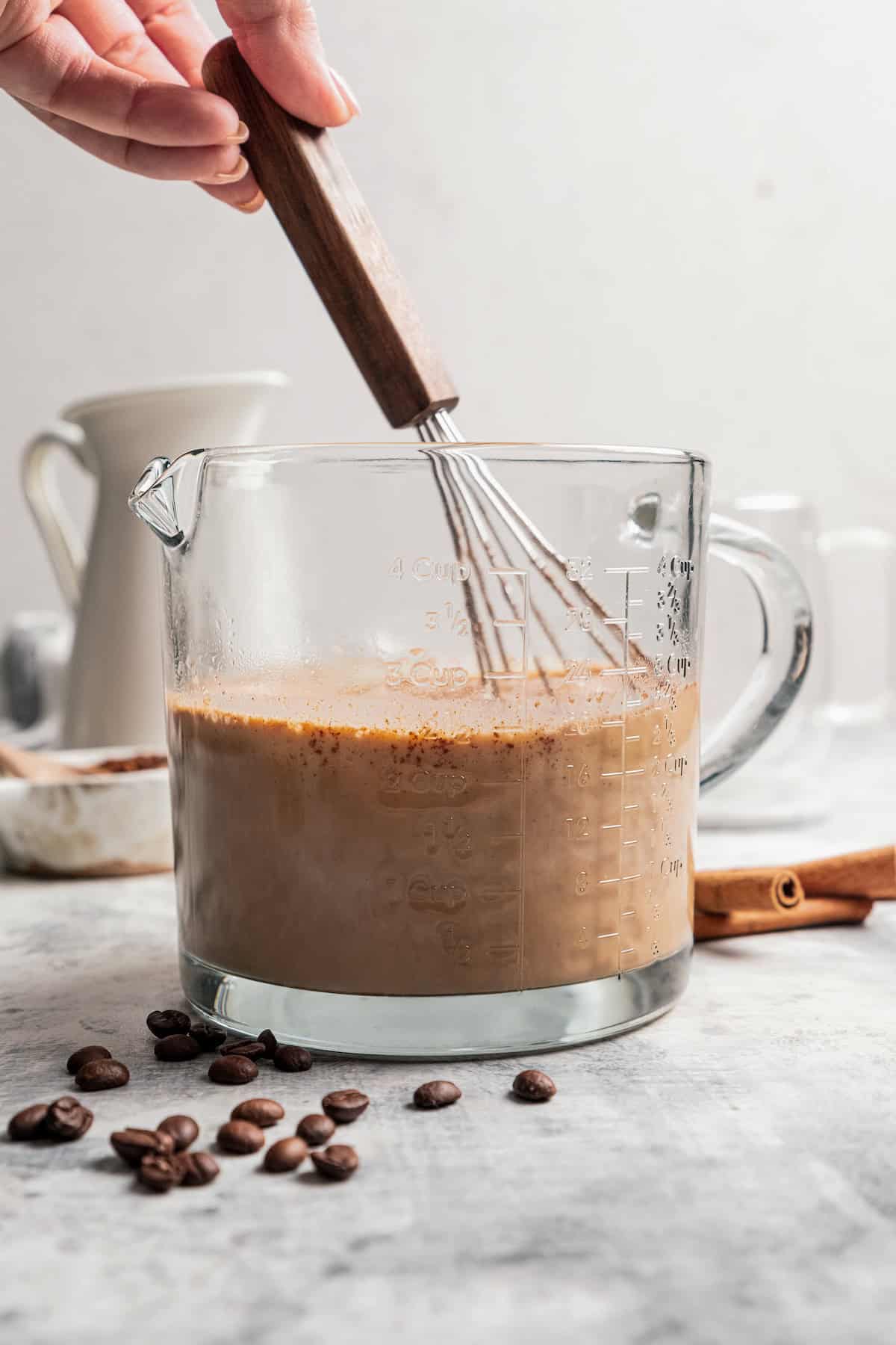 Espresso being whisked into eggnog in a glass mixing bowl.