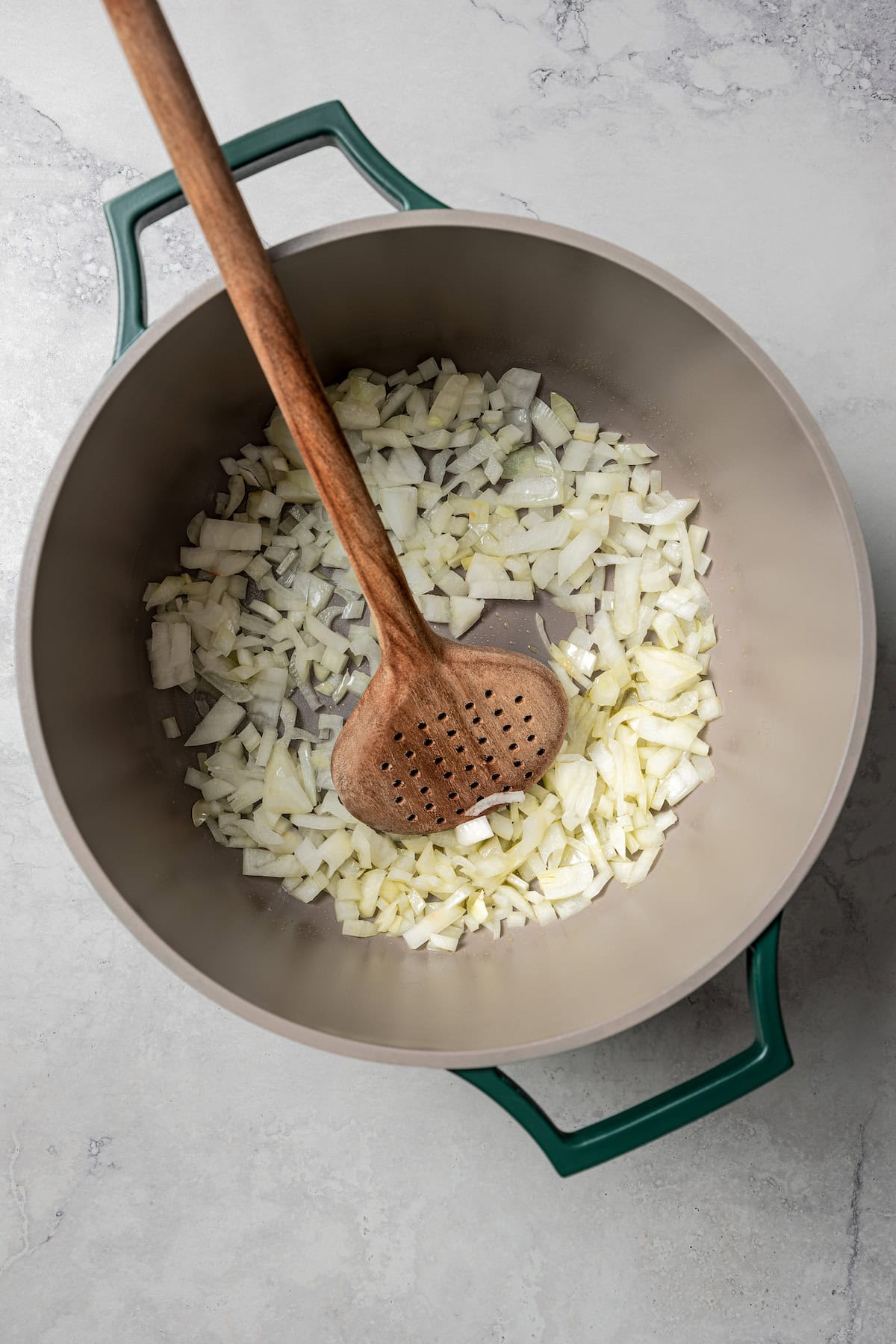 Diced onions sautéing in a large pot with a wooden spoon.