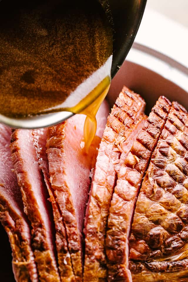 Honey mustard glaze being poured over spiral cut ham slices.