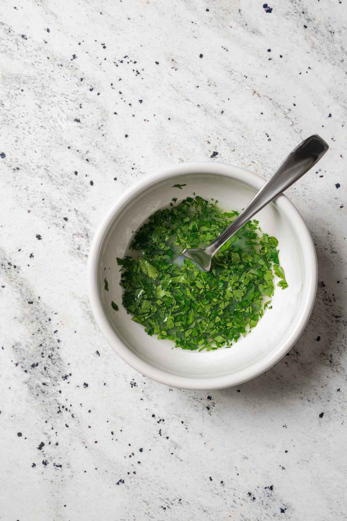 Lemon juice mixed with chopped parsley in a small bowl with a spoon.