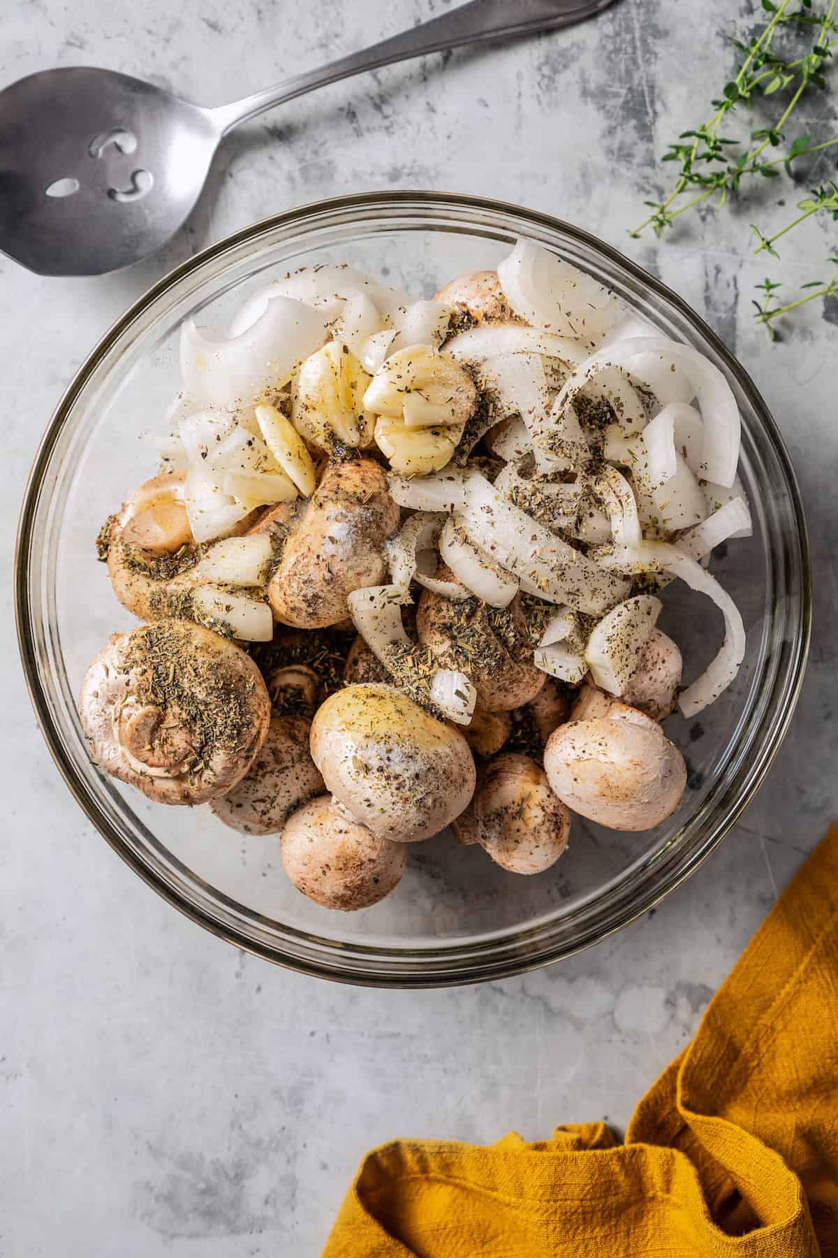 Mushrooms and onions tossed with oil and seasonings in a glass bowl.