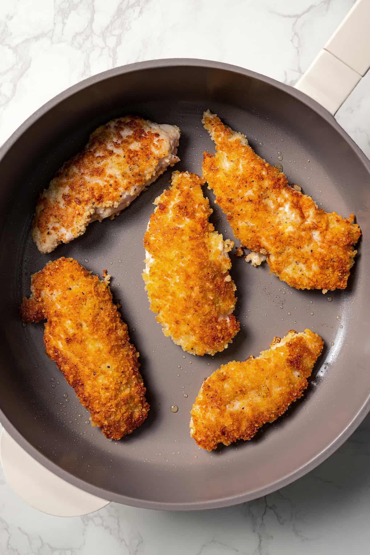 Crispy parmesan chicken tenders in a skillet.