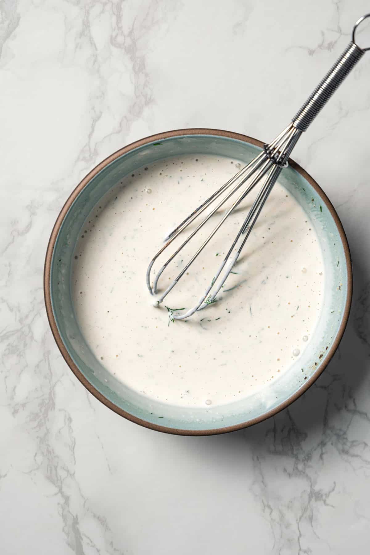 A bowl of buttermilk ranch dressing with a whisk.