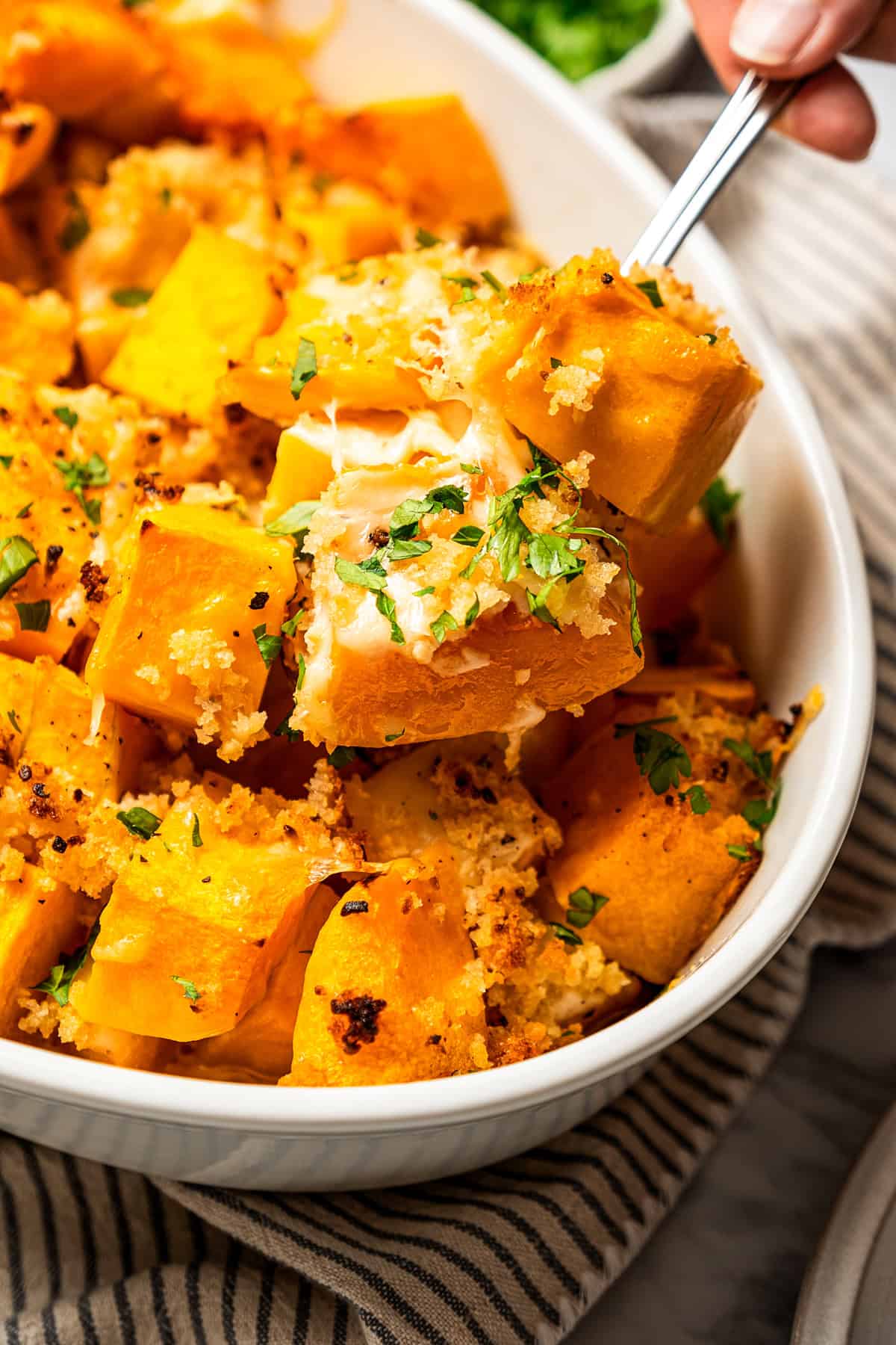 Spooning out baked butternut squash from a casserole dish.