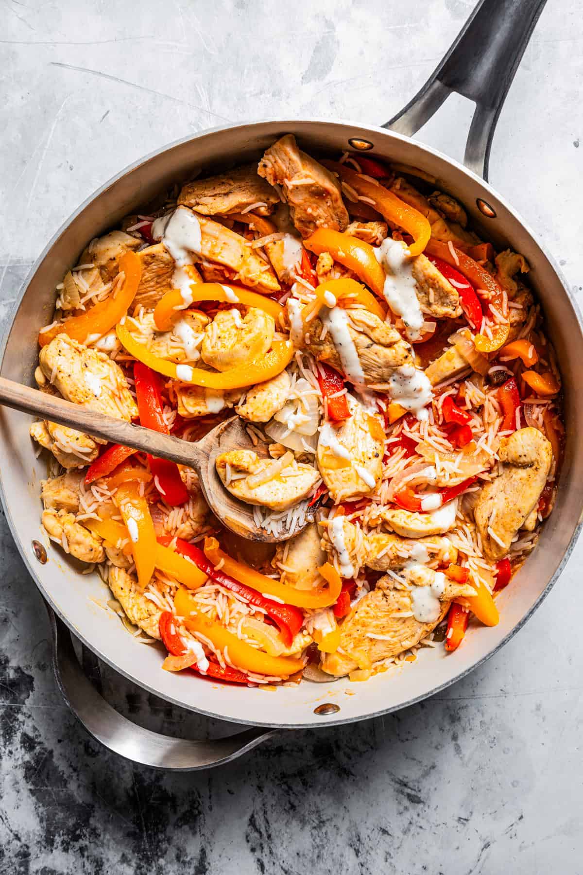 Wooden spoon stirring ranch dressing into a skillet of chicken fajitas.