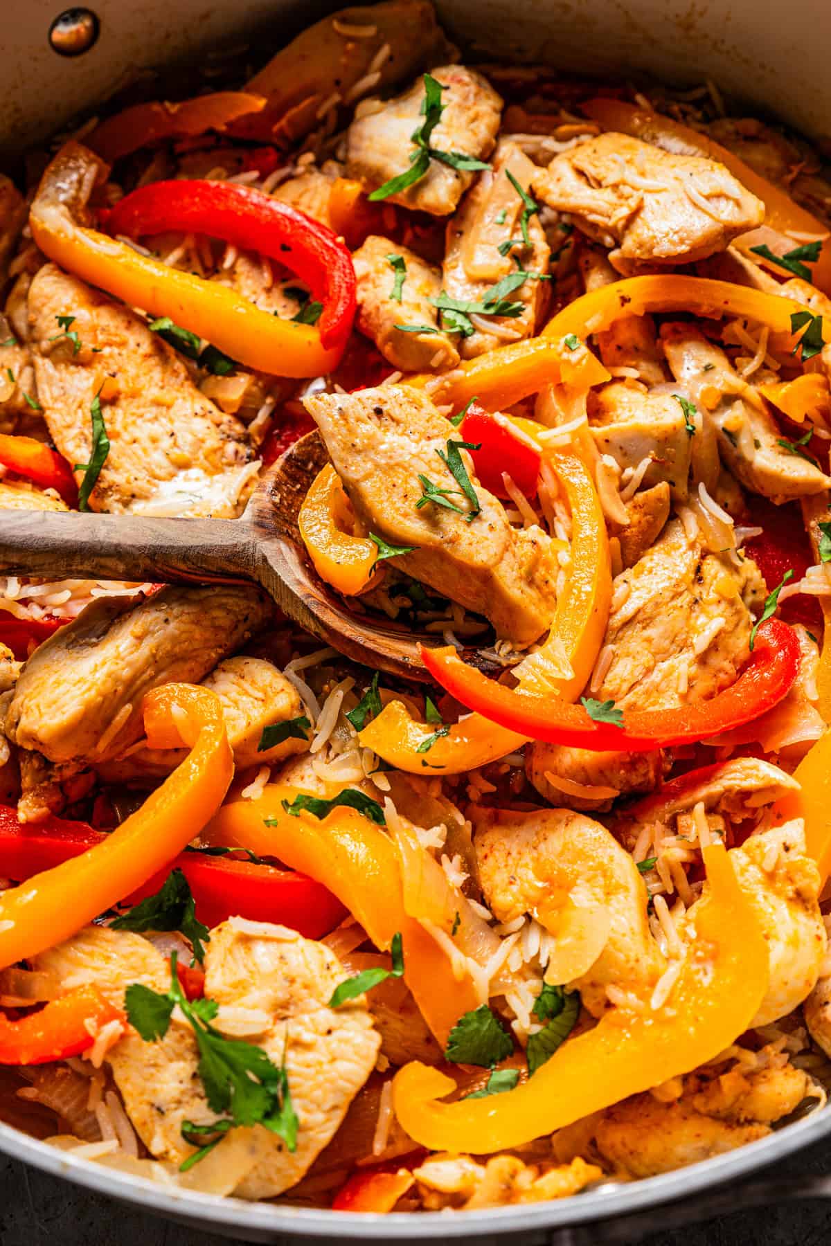 Stirring through sliced bell peppers and cooked chicken in a skillet.