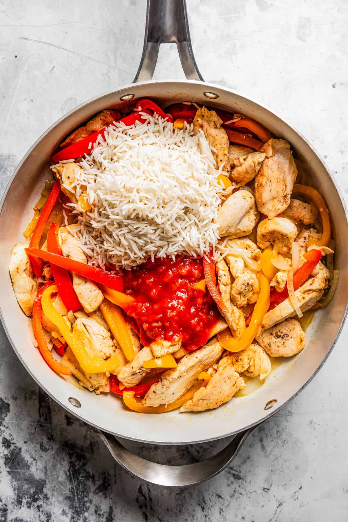 Rice, sliced onions and red and orange bell peppers added to a skillet with cooked chicken.