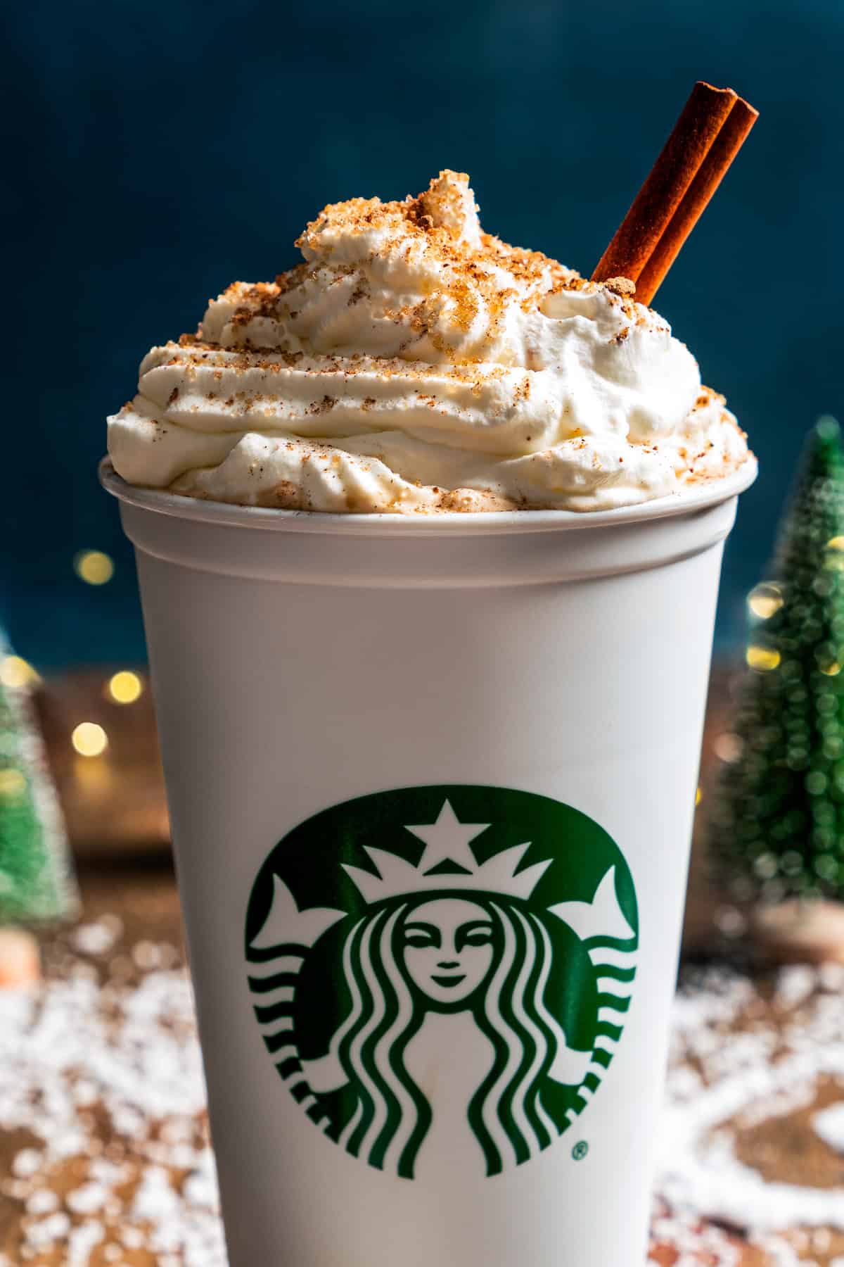 A homemade eggnog latte in a Starbucks cup, garnished with whipped cream, ground nutmeg, and a cinnamon stick.