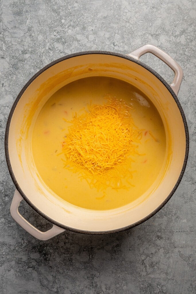 Grated cheese added to beer cheese soup ingredients in a pot.