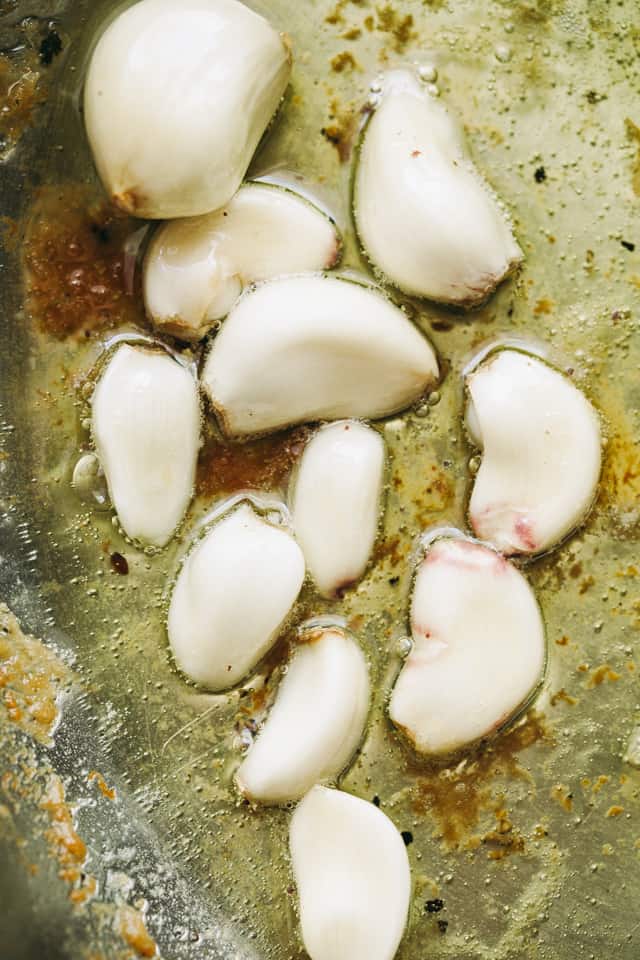 Cooking whole garlic cloves in a skillet with vegetable oil.