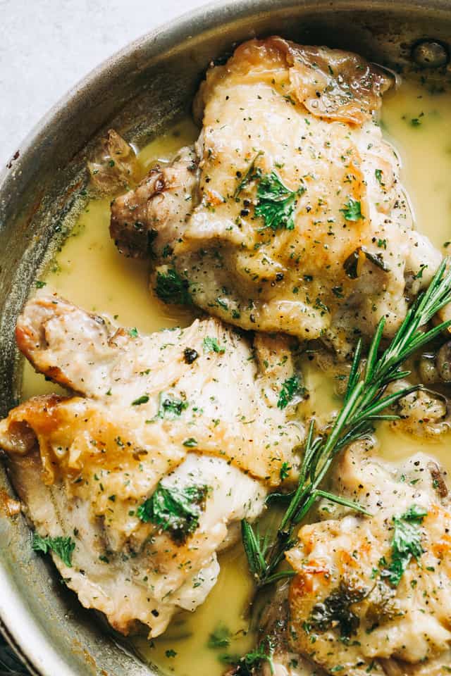 Overhead shot of three bone-in skin-on chicken thighs cooking in a garlic sauce with a rosemary sprig on top of the chicken.