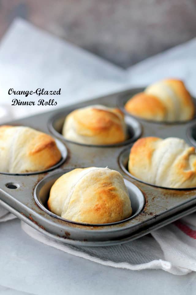 Baked orange dinner rolls in a muffin tin.