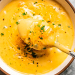 Close up overhead view of a spoonful held over a bowl of beer cheese soup garnished with chopped parsley on a countertop.