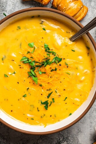 Close-up overhead view of a bowl of beer cheese soup garnished with chopped parsley on a countertop.