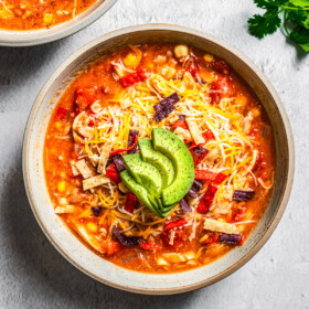 Overhead of chicken tortilla soup served in bowls topped with tortilla strips, cheese, and sliced avocado.