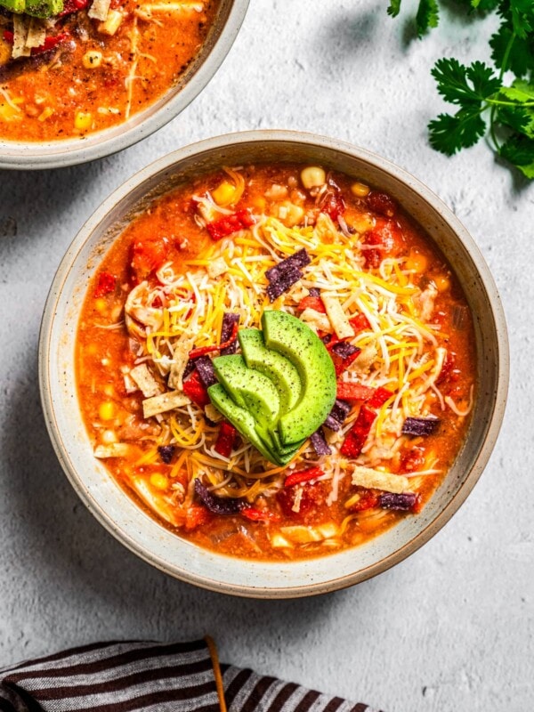 Overhead of chicken tortilla soup served in bowls topped with tortilla strips, cheese, and sliced avocado.
