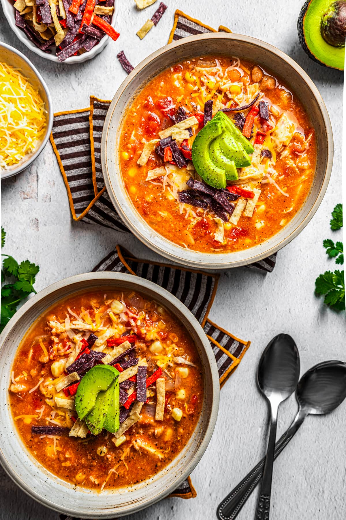 Two bowls of chicken tortilla soup topped with tortilla strips, cheese, and sliced avocado.