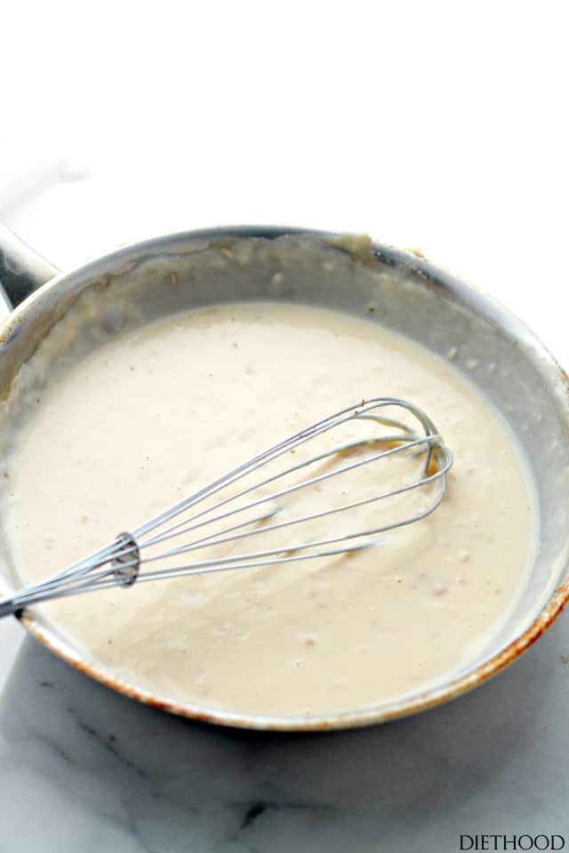 A stainless steel skillet with creamy sauce inside. A whisk is resting in the sauce.