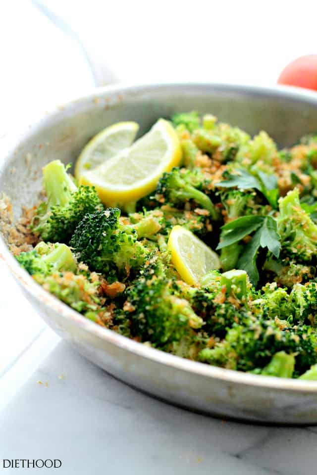 Angled photo of broccoli with lemon wedges and crispy panko in a bowl. 