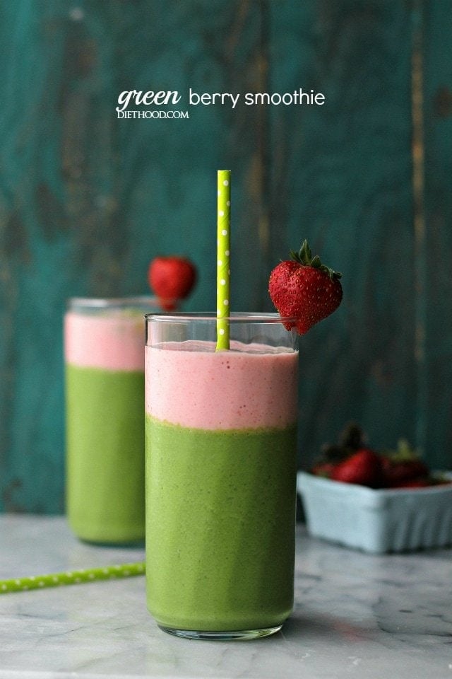 Two glasses with a layer of green and a layer of pink smoothie, and topped with a strawberry and paper straw