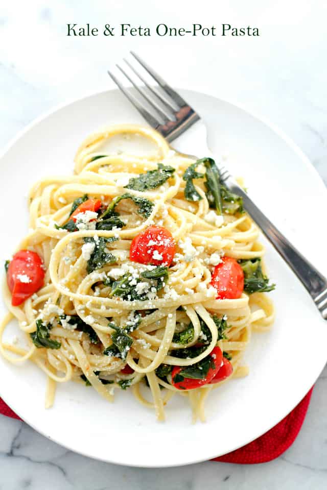 A pile of fettuccine pasta mixed with feta cheese, cherry tomatoes, and kale.