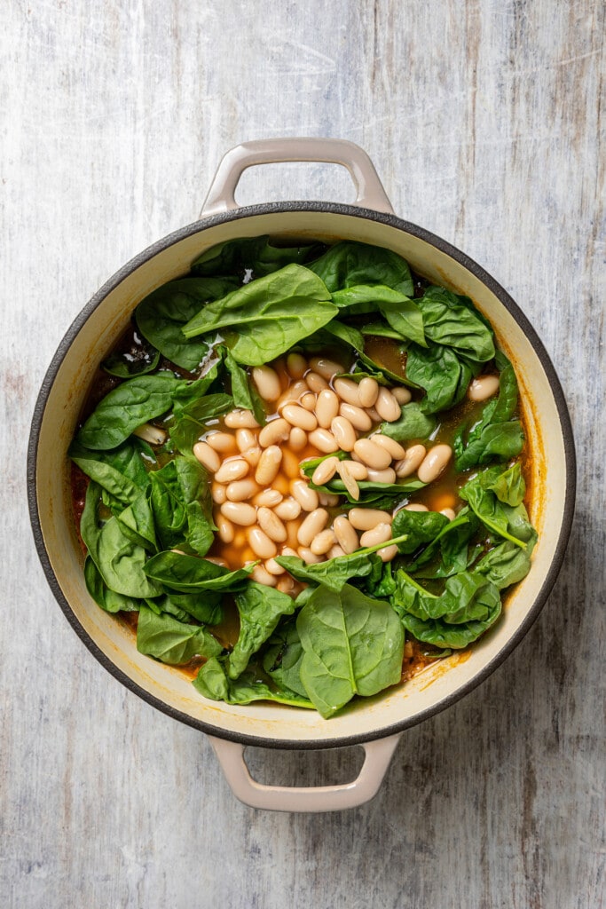 Cannellini beans and baby spinach leaves added to a pot of minestrone soup.