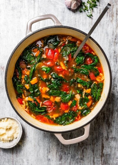 Finished minestrone soup in a large pot with a ladle, surrounded by soup ingredients.