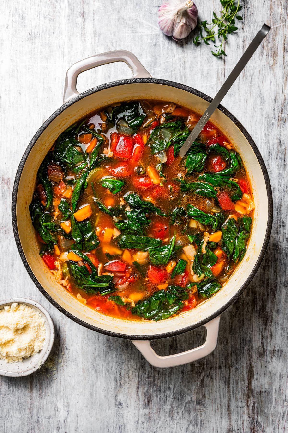 Finished minestrone soup in a large pot with a ladle, surrounded by soup ingredients.