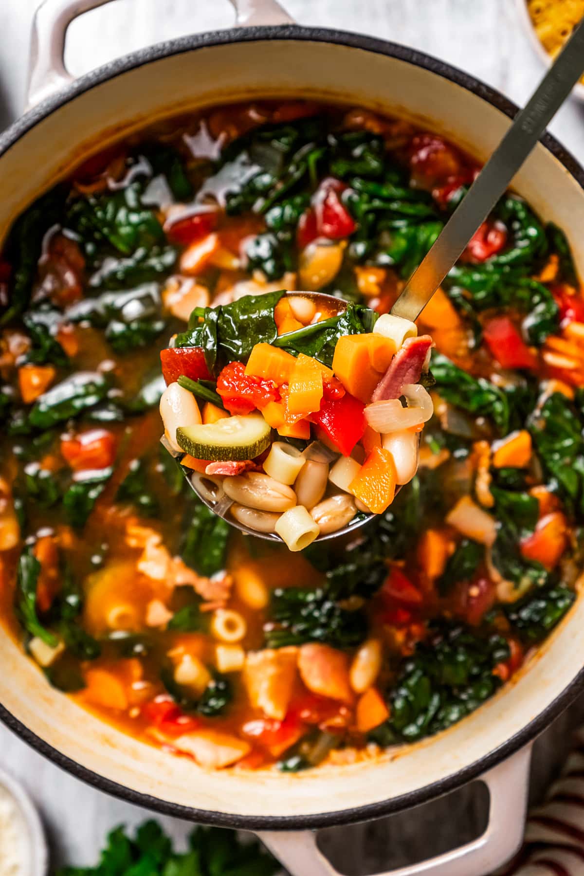 A ladle full of minestrone soup held over a large pot of soup.