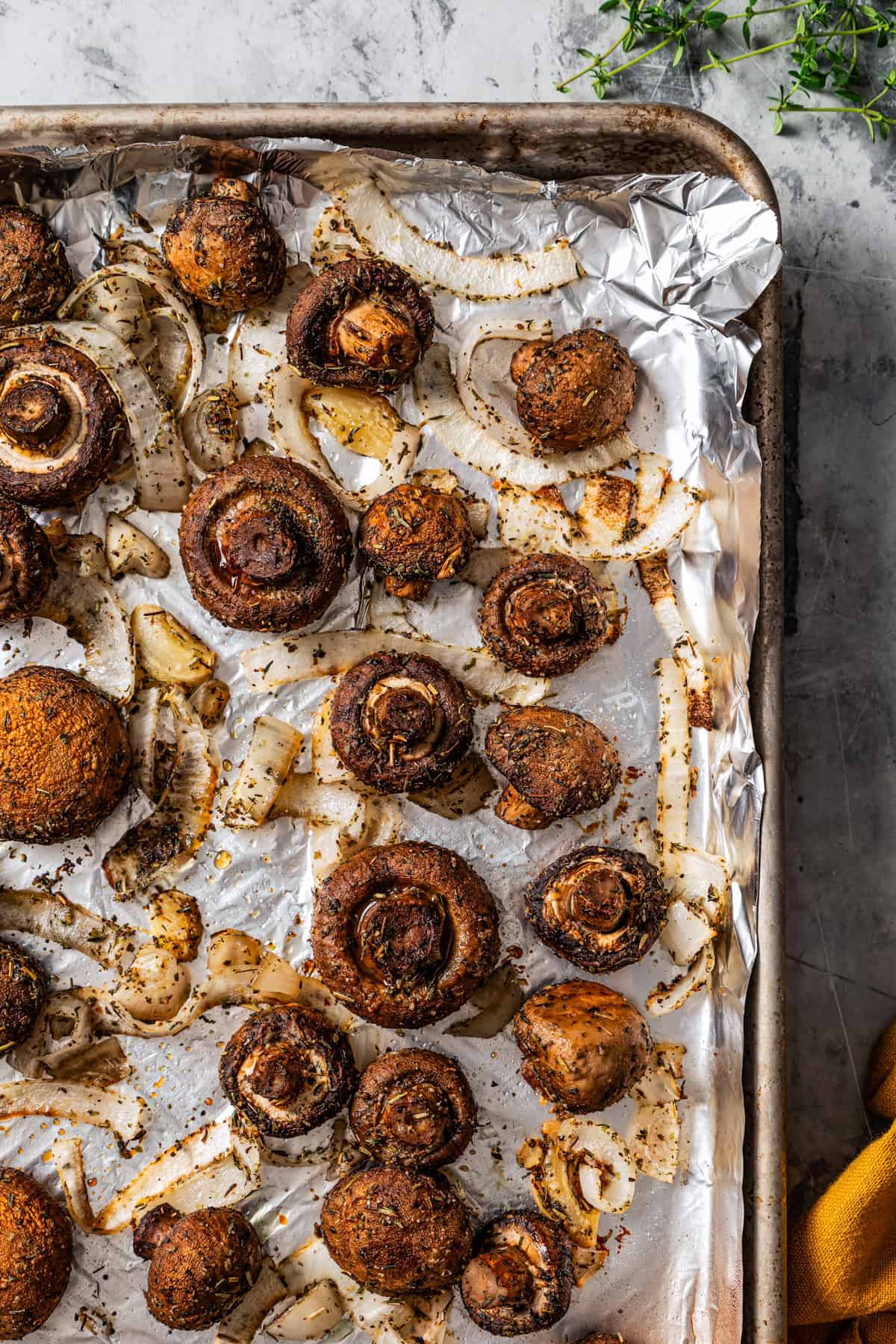 Freshly roasted mushrooms and onions on a lined baking sheet.