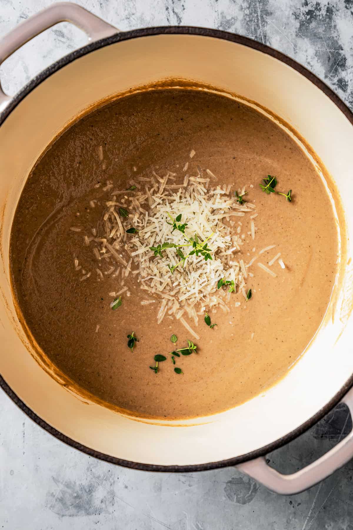 Overhead view of creamy mushroom soup in a large pot garnished with shredded parmesan and fresh herbs.