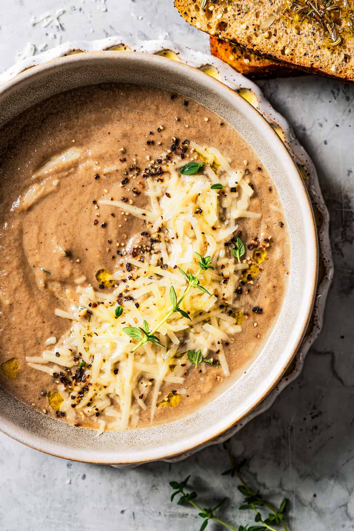 Overhead view of creamy mushroom soup in a bowl garnished with shredded parmesan and fresh herbs.