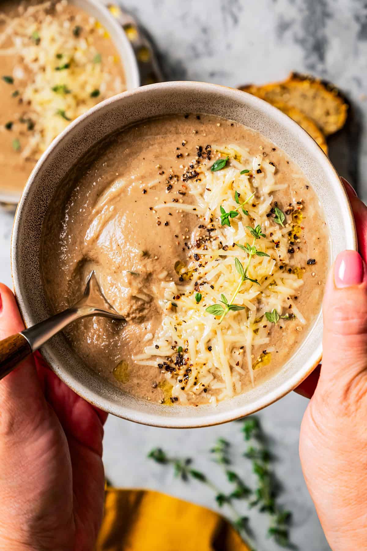 Weekly Menu Plan Two hands holding up a bowl of creamy mushroom soup garnished with shredded parmesan and fresh herbs.