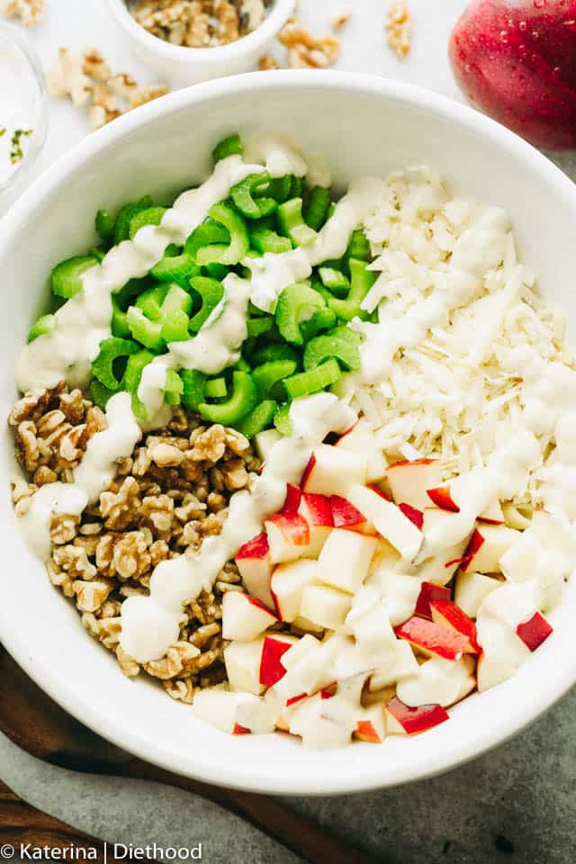 A large salad bowl with chopped apples, sliced celery, chopped walnuts, and cheese topped with a drizzle of creamy dressing.
