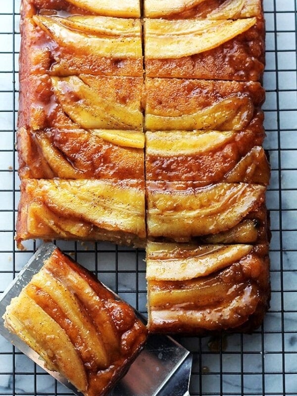 Banana upside down cake on a cooling wrack with a spatula taking a slice away.