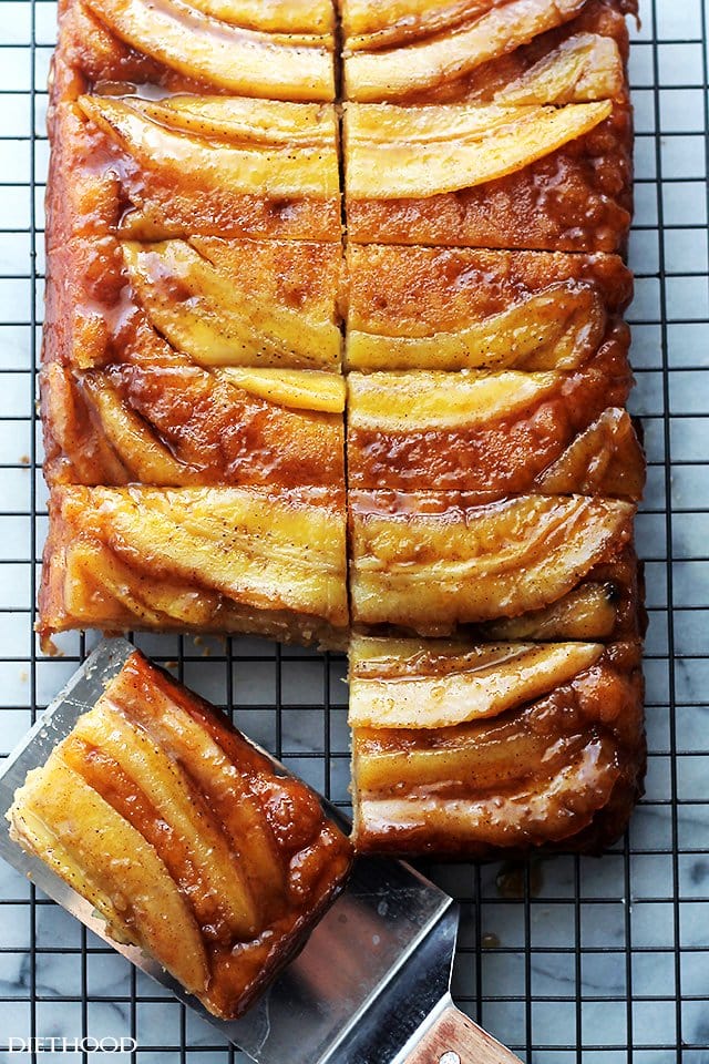 Banana upside down cake on a cooling wrack with a spatula taking a slice away.