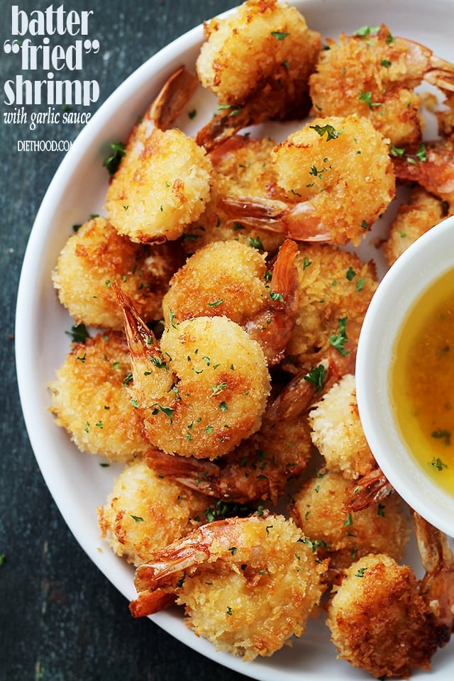 Battered baked shrimp on a plate with dipping sauce in a bowl. 