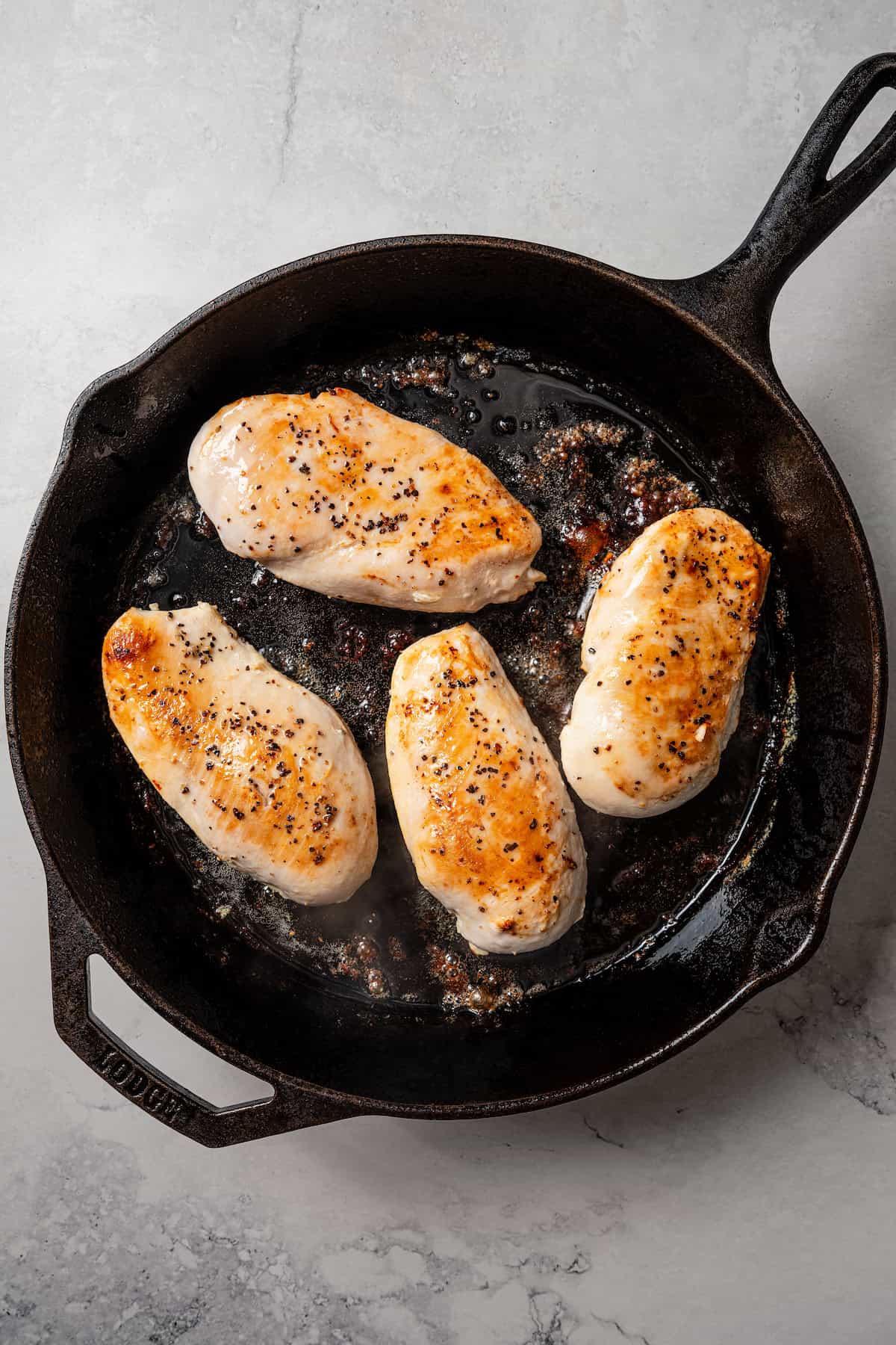 Four seared chicken breasts in a cast iron skillet.