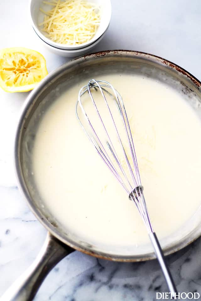 Overhead view of lemon cream sauce in a skillet with a whisk, next to a bowl of parmesan.