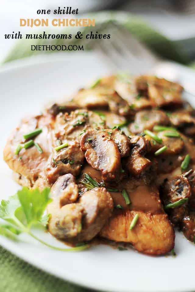 A plate of two chicken breasts topped with dijon cream sauce, mushrooms, and chives.
