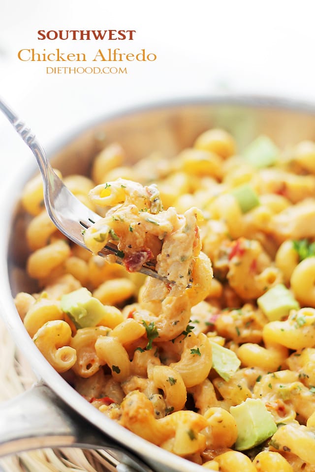 A fork with chicken, vegetables, and pasta on it over a pan of chicken alfredo