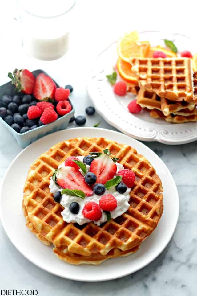 Cream cheese waffles served on two plates with a small basket of fresh berries set on the side.