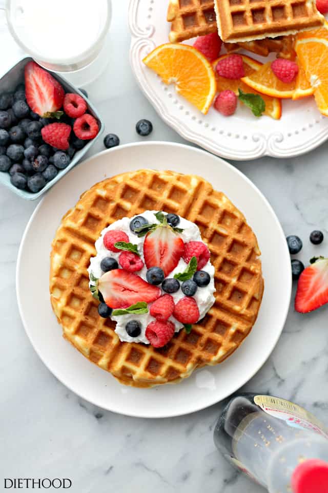 A photo of waffles on a plate. They are topped with whipped cream and fresh strawberries, blueberries, and raspberries.