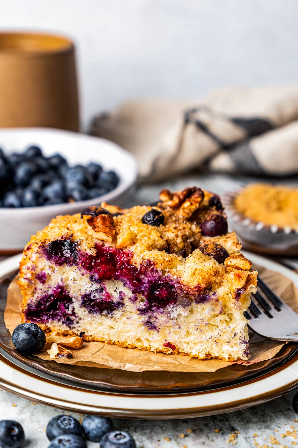 A slice of cake served on a plate with a bowl of blueberries in the background.