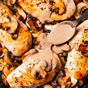 A spoon drizzling Dijon mushroom sauce over chicken Dijon in a cast iron skillet.