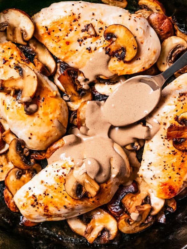 A spoon drizzling Dijon mushroom sauce over chicken Dijon in a cast iron skillet.