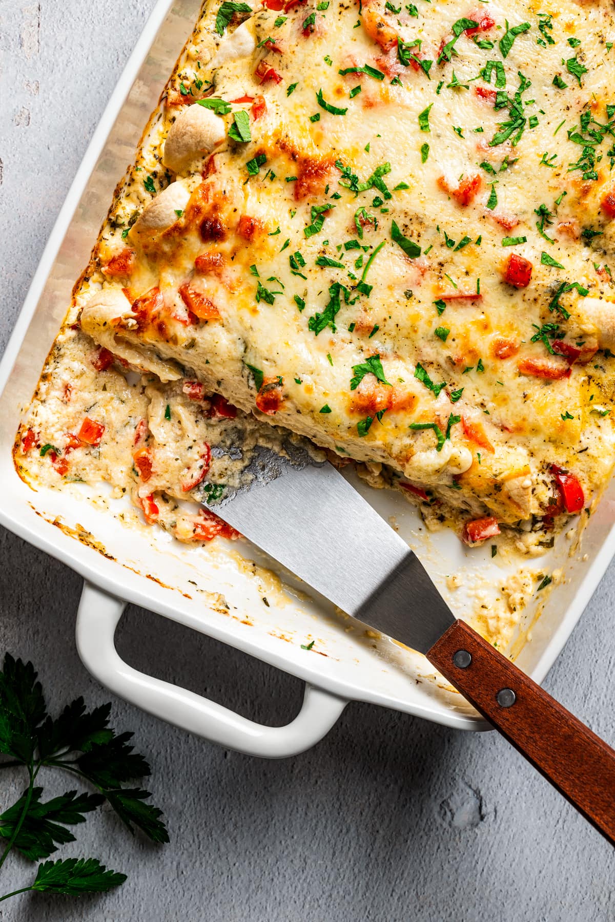 Overhead image of serving chicken enchilada casserole with a metal spatula.