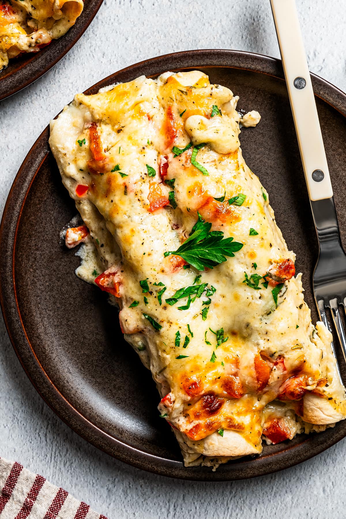 Photo of chicken enchilada casserole served on a dark-colored plate with a fork set next to the enchiladas.