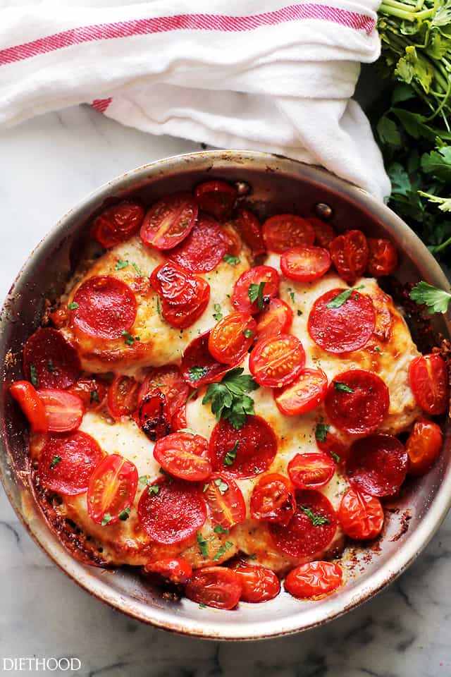 An overhead image of four chicken breasts in a skillet, topped with melted cheese, pepperoni, and tomatoes.